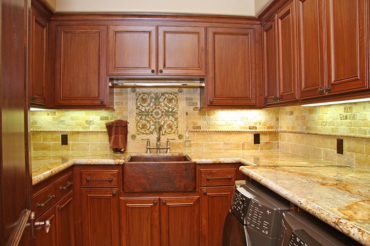 Design ideas for a medium sized mediterranean u-shaped separated utility room in Sacramento with a belfast sink, recessed-panel cabinets, medium wood cabinets, granite worktops, beige walls, limestone flooring and a side by side washer and dryer.