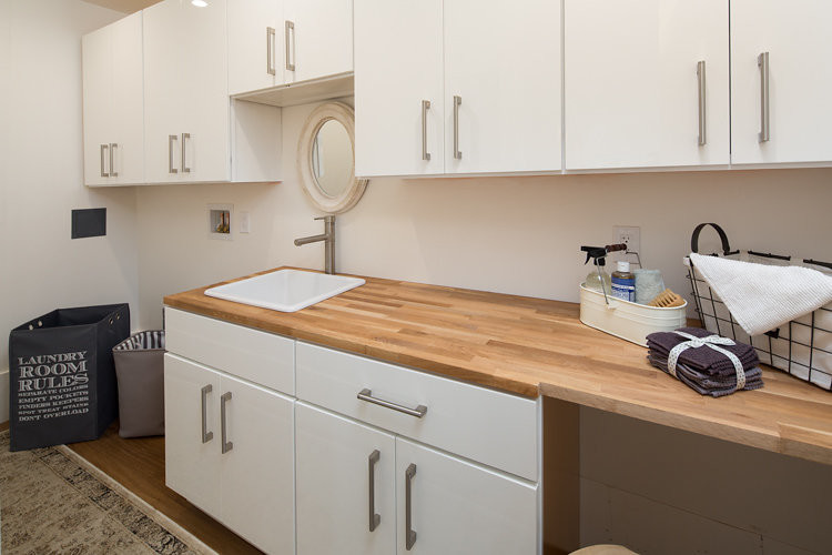 Einzeilige, Große Industrial Waschküche mit Einbauwaschbecken, flächenbündigen Schrankfronten, weißen Schränken, Arbeitsplatte aus Holz, weißer Wandfarbe und braunem Holzboden in San Francisco