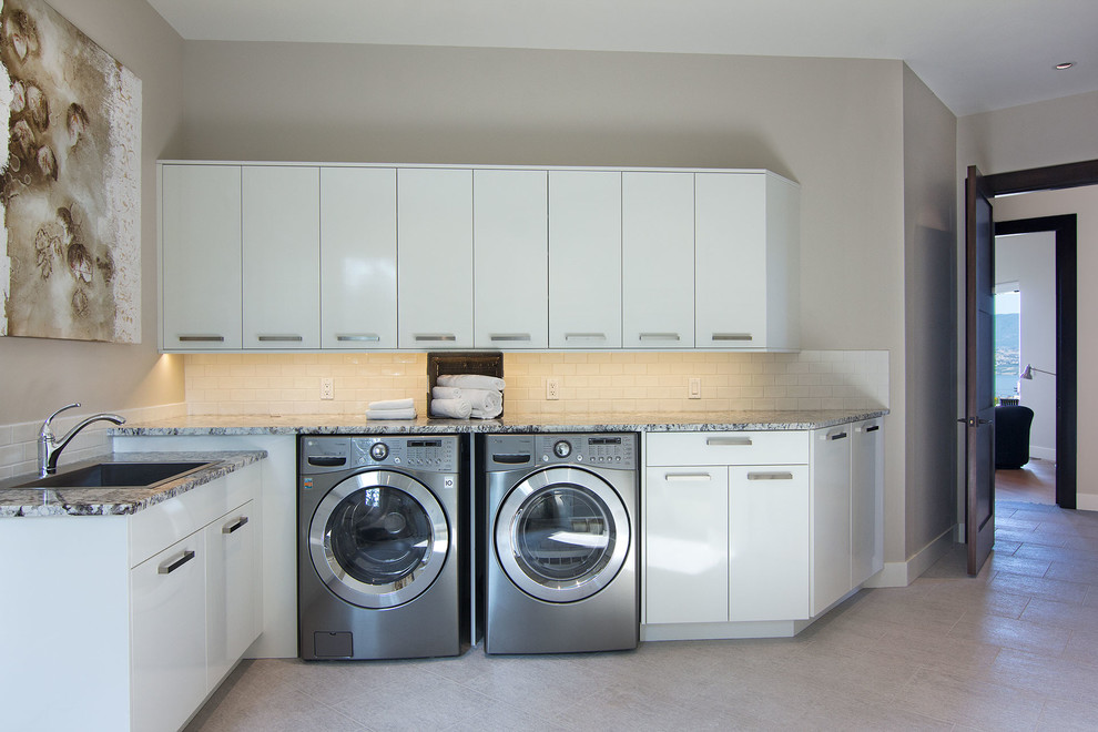 Contemporary laundry room in Vancouver with beige walls, a drop-in sink, white cabinets and grey floor.