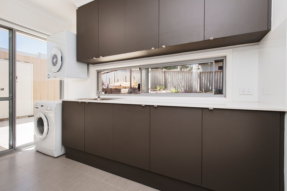 Design ideas for a medium sized contemporary single-wall separated utility room in Perth with a built-in sink, flat-panel cabinets, brown cabinets, composite countertops, white walls and a stacked washer and dryer.