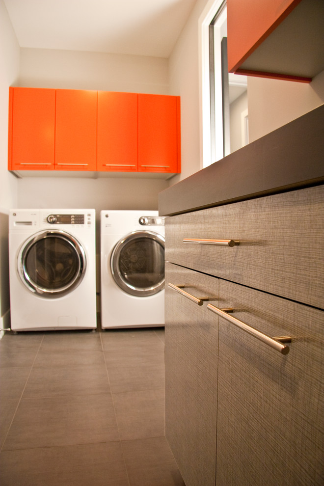 Einzeilige, Kleine Moderne Waschküche mit flächenbündigen Schrankfronten, orangefarbenen Schränken, Laminat-Arbeitsplatte, Waschmaschine und Trockner nebeneinander und schwarzer Arbeitsplatte in Grand Rapids