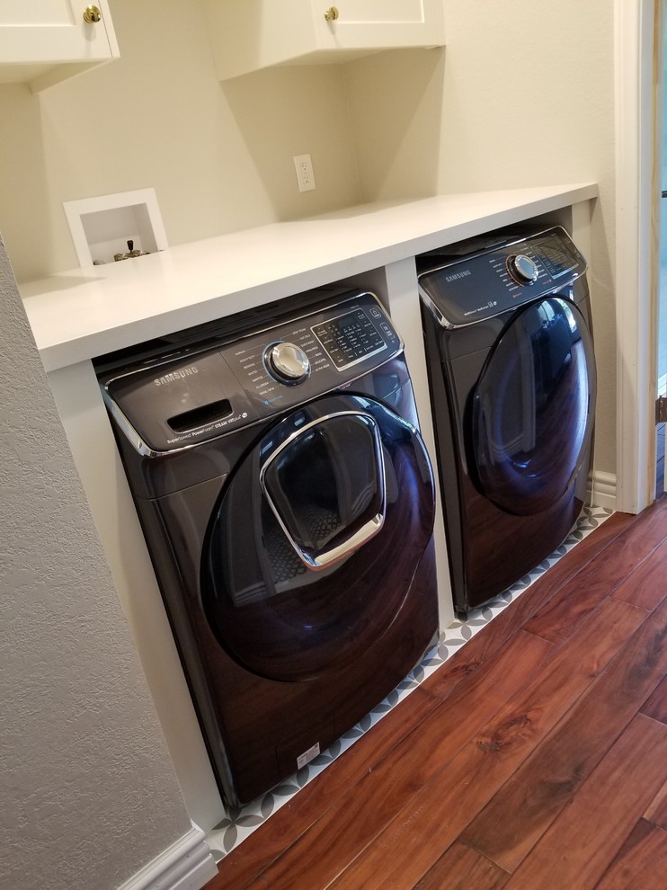 This is an example of a small modern single-wall laundry cupboard in Los Angeles with shaker cabinets, white cabinets, composite countertops, beige walls, medium hardwood flooring, a side by side washer and dryer, brown floors and white worktops.