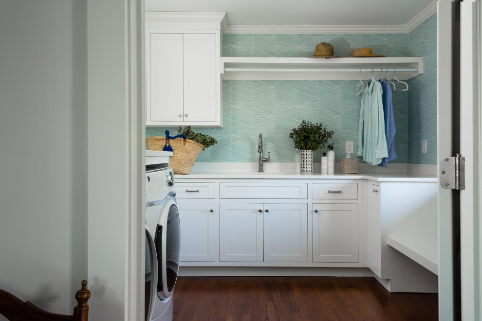 プロビデンスにある高級な広いビーチスタイルのおしゃれな洗濯室 (コの字型、アンダーカウンターシンク、シェーカースタイル扉のキャビネット、クオーツストーンカウンター、白いキッチンパネル、クオーツストーンのキッチンパネル、青い壁、濃色無垢フローリング、左右配置の洗濯機・乾燥機、茶色い床、白いキッチンカウンター、壁紙) の写真