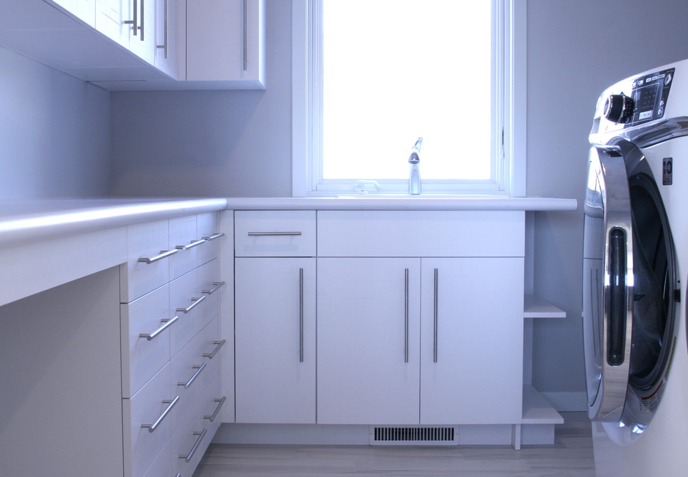 Foto på en mellanstor funkis l-formad tvättstuga enbart för tvätt, med släta luckor, vita skåp, grå väggar och en tvättmaskin och torktumlare bredvid varandra