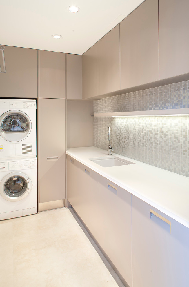 Moderner Hauswirtschaftsraum in L-Form mit Unterbauwaschbecken, flächenbündigen Schrankfronten, grauen Schränken, Waschmaschine und Trockner gestapelt und weißer Arbeitsplatte in Vancouver