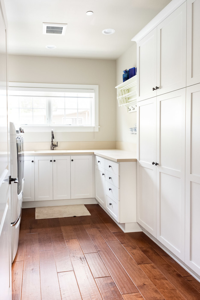 This is an example of a medium sized traditional u-shaped separated utility room in San Luis Obispo with a built-in sink, shaker cabinets, white cabinets, granite worktops, beige walls, dark hardwood flooring, a side by side washer and dryer, brown floors and beige worktops.