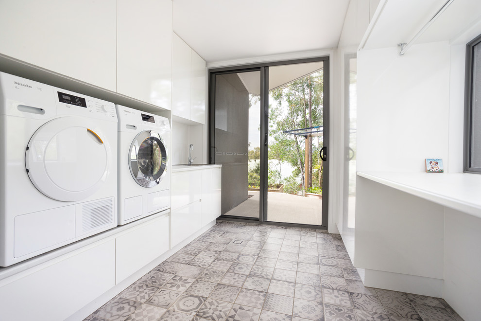 Inspiration for a large contemporary galley utility room in Sunshine Coast with a single-bowl sink, white cabinets, laminate countertops, white walls, concrete flooring and a side by side washer and dryer.