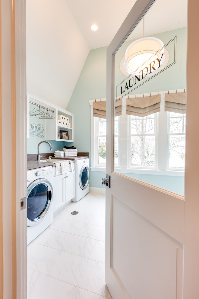 Photo of a large beach style utility room in Other with a built-in sink, recessed-panel cabinets, white cabinets, laminate countertops, blue walls, marble flooring and a side by side washer and dryer.