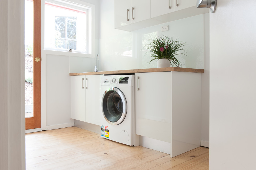 Immagine di una lavanderia multiuso tradizionale di medie dimensioni con lavello da incasso, ante bianche, top in legno, parquet chiaro e ante lisce
