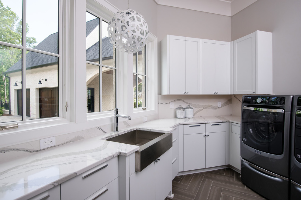 Exempel på en stor modern vita u-formad vitt tvättstuga enbart för tvätt, med en rustik diskho, vita skåp, bänkskiva i kvarts, grå väggar, en tvättmaskin och torktumlare bredvid varandra, släta luckor och brunt golv