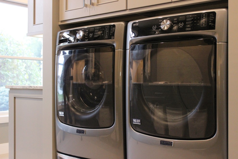 シカゴにある広いトランジショナルスタイルのおしゃれな洗濯室 (L型、アンダーカウンターシンク、フラットパネル扉のキャビネット、グレーのキャビネット、クオーツストーンカウンター、グレーの壁、セラミックタイルの床、左右配置の洗濯機・乾燥機) の写真