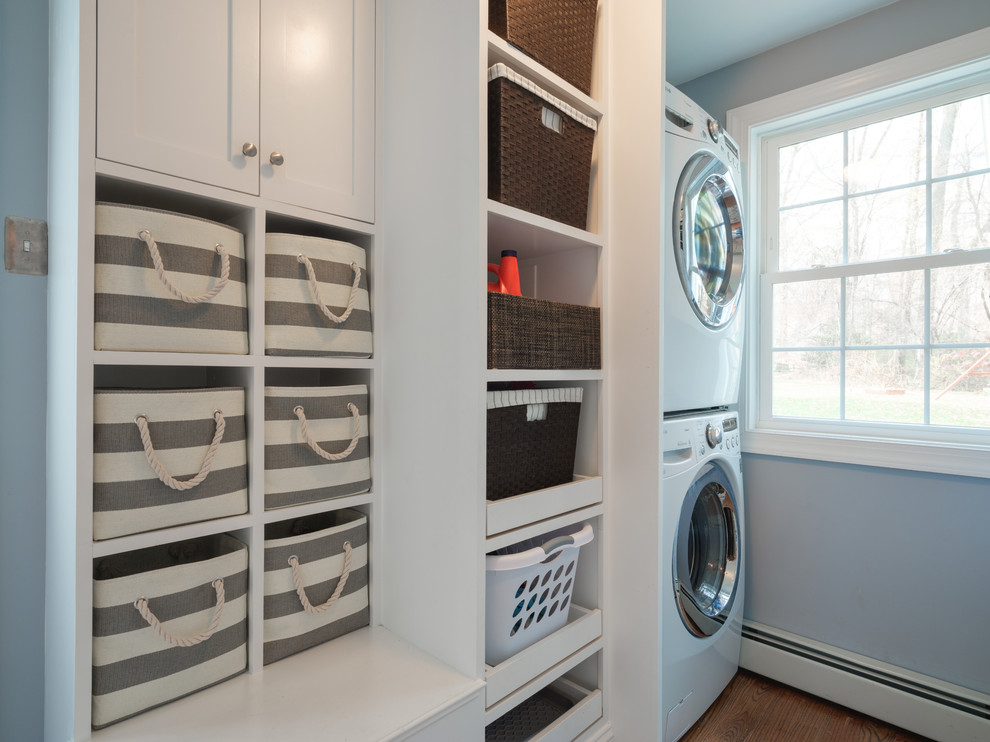 Foto di una sala lavanderia design con ante in stile shaker, ante bianche, pareti blu, pavimento in legno massello medio, lavatrice e asciugatrice a colonna e pavimento marrone