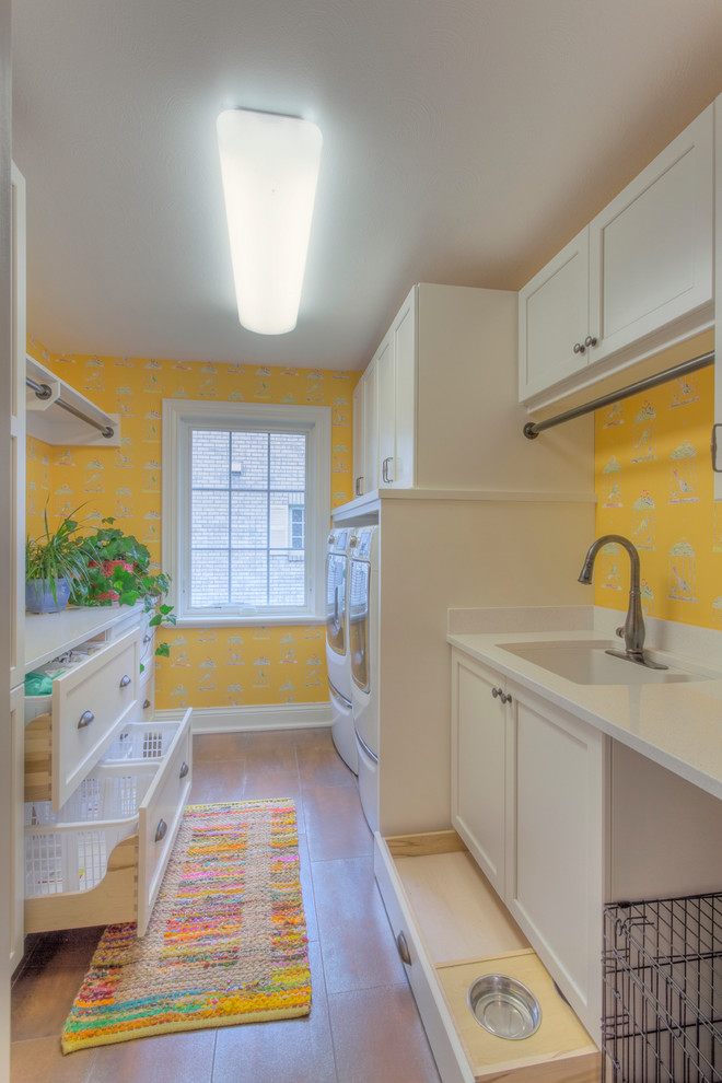 Idéer för en stor klassisk parallell tvättstuga enbart för tvätt, med gula väggar, klinkergolv i keramik, en undermonterad diskho, vita skåp, bänkskiva i kvarts, en tvättmaskin och torktumlare bredvid varandra och luckor med infälld panel