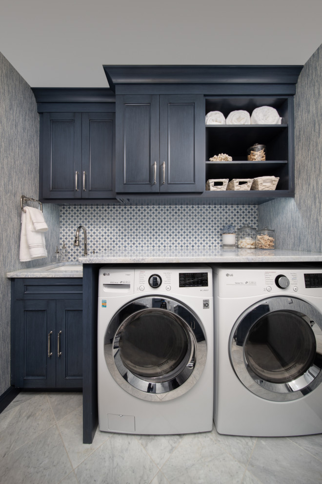 他の地域にある小さなトランジショナルスタイルのおしゃれな洗濯室 (青いキャビネット、左右配置の洗濯機・乾燥機、グレーのキッチンカウンター、壁紙、ll型、ドロップインシンク、インセット扉のキャビネット、大理石カウンター、マルチカラーのキッチンパネル、磁器タイルのキッチンパネル、青い壁、大理石の床、白い床) の写真