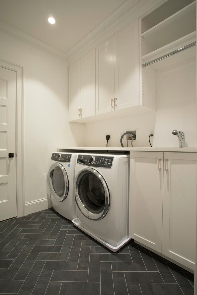 Idéer för mellanstora funkis linjära vitt tvättstugor enbart för tvätt, med en undermonterad diskho, skåp i shakerstil, vita skåp, bänkskiva i kvarts, vita väggar, vinylgolv, en tvättmaskin och torktumlare bredvid varandra och svart golv