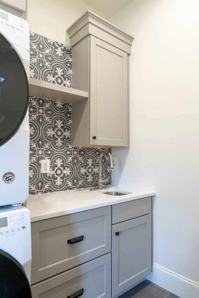ボルチモアにあるカントリー風のおしゃれなランドリールーム (I型、グレーのキャビネット、上下配置の洗濯機・乾燥機、白いキッチンカウンター、セメントタイルのキッチンパネル) の写真