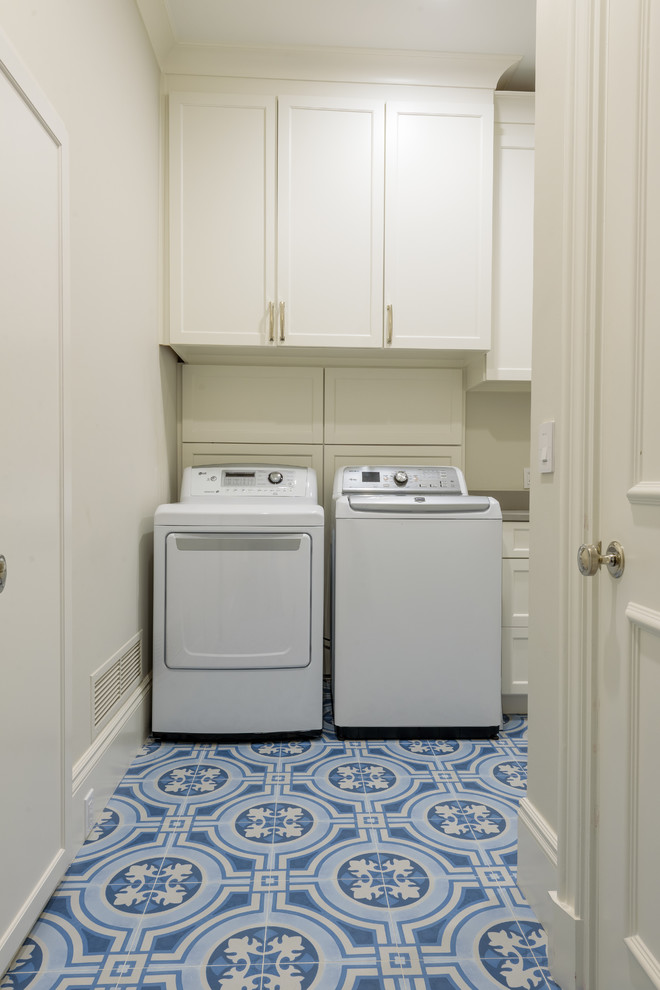 Bild på en stor vintage grå l-formad grått tvättstuga enbart för tvätt, med en undermonterad diskho, luckor med infälld panel, vita skåp, bänkskiva i kvarts, vita väggar, klinkergolv i keramik, en tvättmaskin och torktumlare bredvid varandra och blått golv