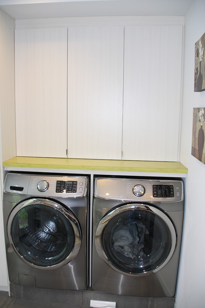 Inredning av en modern mellanstor parallell tvättstuga enbart för tvätt, med en dubbel diskho, släta luckor, grå skåp, laminatbänkskiva, grå väggar, klinkergolv i keramik och en tvättmaskin och torktumlare bredvid varandra