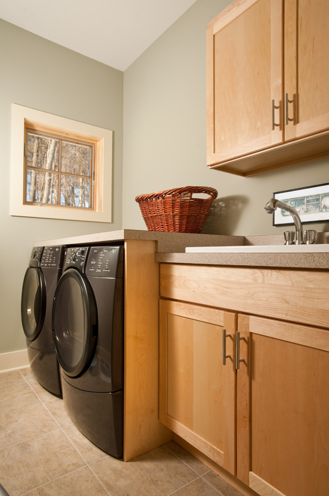 Inredning av en modern mellanstor beige linjär beige tvättstuga enbart för tvätt, med en nedsänkt diskho, skåp i shakerstil, laminatbänkskiva, klinkergolv i porslin, en tvättmaskin och torktumlare bredvid varandra, beiget golv, skåp i ljust trä och gröna väggar
