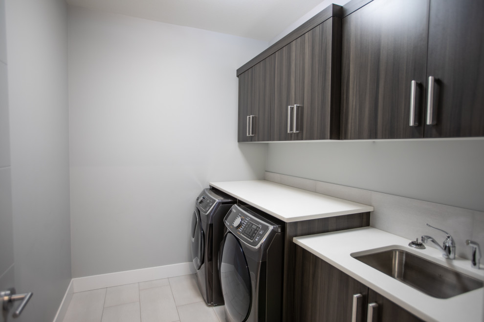 Einzeilige, Mittelgroße Moderne Waschküche mit Unterbauwaschbecken, flächenbündigen Schrankfronten, dunklen Holzschränken, Quarzwerkstein-Arbeitsplatte, grauer Wandfarbe, Porzellan-Bodenfliesen, Waschmaschine und Trockner nebeneinander, beigem Boden und weißer Arbeitsplatte in Vancouver