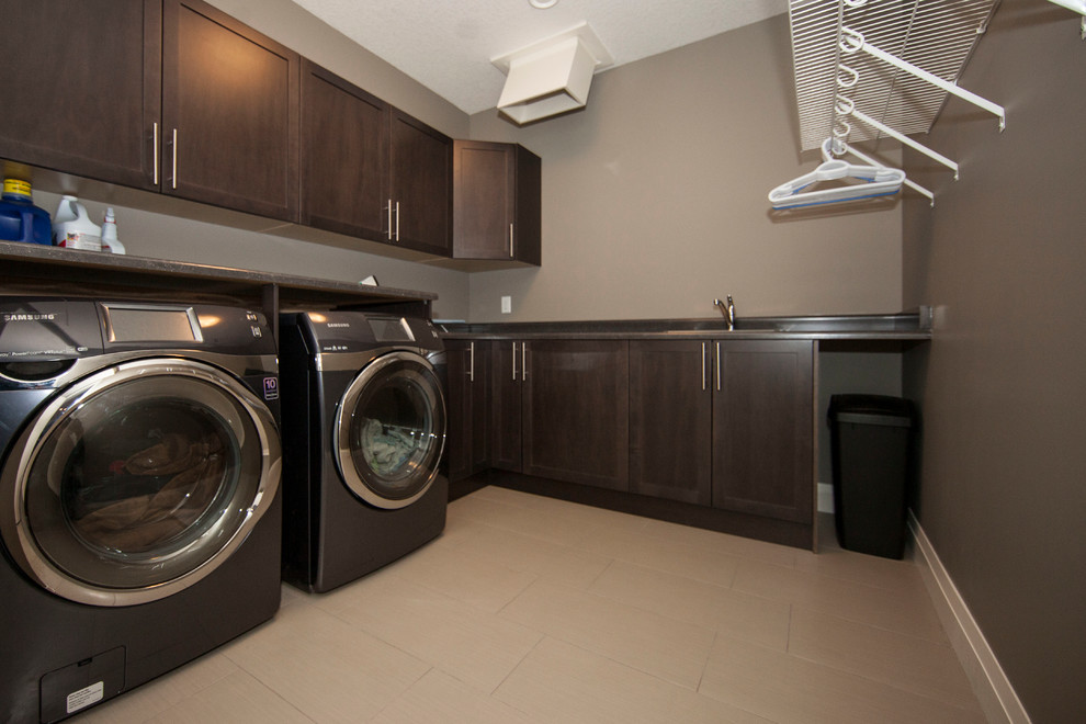 Large trendy l-shaped ceramic tile dedicated laundry room photo in Edmonton with a drop-in sink, recessed-panel cabinets, dark wood cabinets, laminate countertops, gray walls and a side-by-side washer/dryer