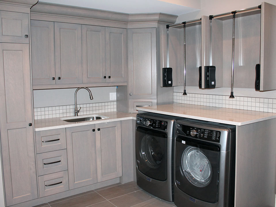 Bild på en mellanstor funkis l-formad tvättstuga enbart för tvätt, med en undermonterad diskho, skåp i shakerstil, grå skåp, grå väggar och en tvättmaskin och torktumlare bredvid varandra
