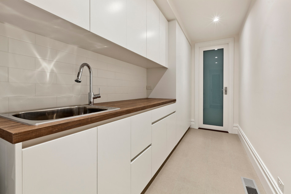 Einzeilige Moderne Waschküche mit Einbauwaschbecken, flächenbündigen Schrankfronten, weißen Schränken, Arbeitsplatte aus Holz, weißer Wandfarbe und Keramikboden in Melbourne