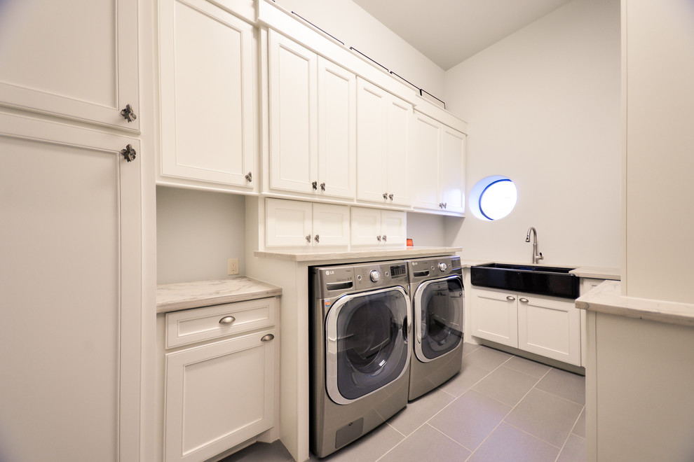 Design ideas for a large contemporary u-shaped utility room in Houston with a belfast sink, shaker cabinets, white cabinets, marble worktops, white walls, a side by side washer and dryer, grey floors and white worktops.