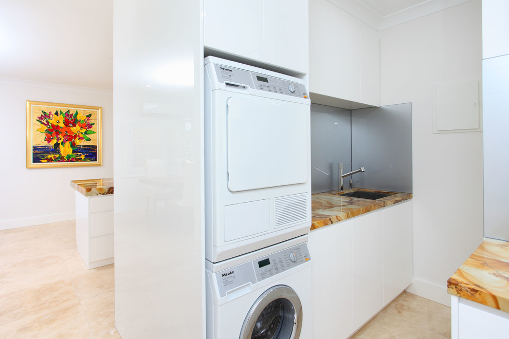 Moderner Hauswirtschaftsraum mit Onyx-Arbeitsplatte, Waschmaschine und Trockner gestapelt, beigem Boden und bunter Arbeitsplatte in Brisbane