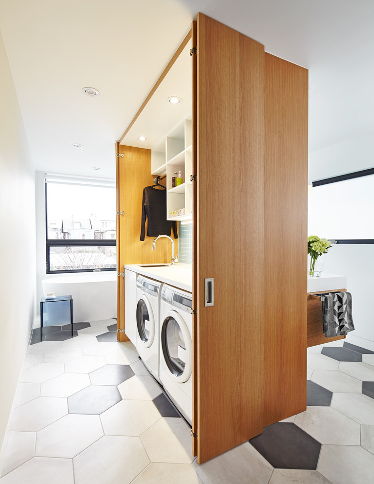 Modelo de armario lavadero lineal actual pequeño con armarios con paneles lisos, paredes blancas, lavadora y secadora juntas y puertas de armario de madera oscura