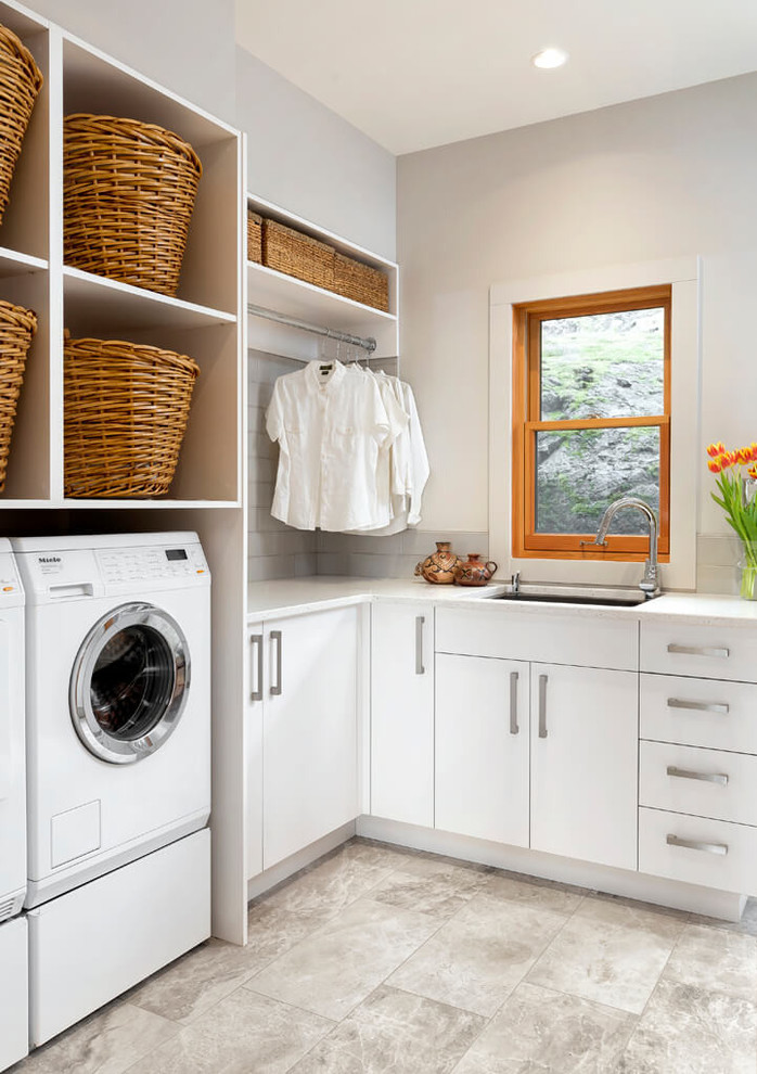 Inspiration för moderna l-formade tvättstugor enbart för tvätt, med en undermonterad diskho, släta luckor, vita skåp, grå väggar, en tvättmaskin och torktumlare bredvid varandra och grått golv