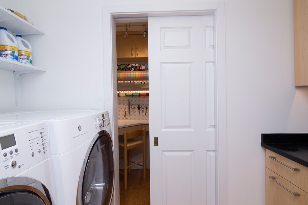 Example of a small trendy galley medium tone wood floor and orange floor dedicated laundry room design in Raleigh with an undermount sink, flat-panel cabinets, light wood cabinets, soapstone countertops, white walls, a side-by-side washer/dryer and black countertops