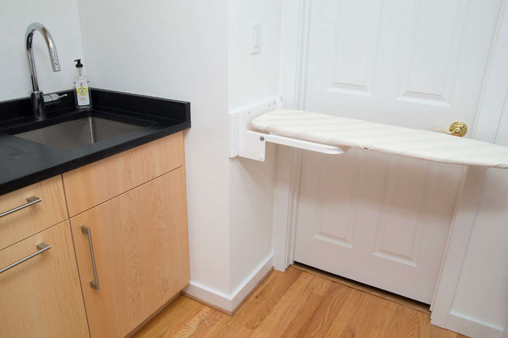 Inspiration för små moderna parallella svart tvättstugor enbart för tvätt, med en undermonterad diskho, släta luckor, skåp i ljust trä, bänkskiva i täljsten, vita väggar, mellanmörkt trägolv, en tvättmaskin och torktumlare bredvid varandra och orange golv