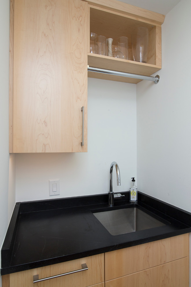 Example of a small trendy galley medium tone wood floor and orange floor dedicated laundry room design in Raleigh with an undermount sink, flat-panel cabinets, light wood cabinets, soapstone countertops, white walls, a side-by-side washer/dryer and black countertops