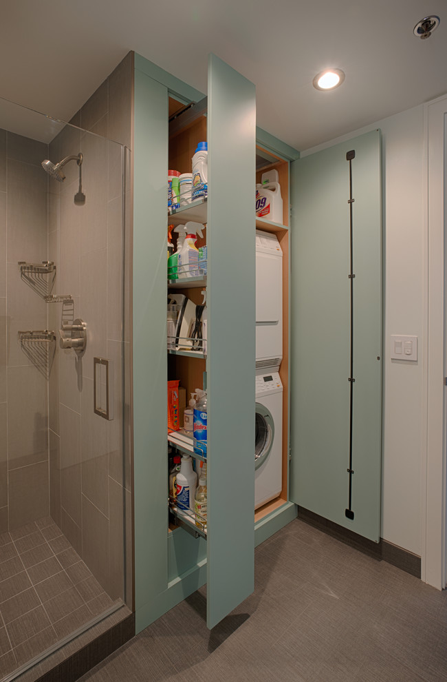 This is an example of a contemporary utility room in San Francisco with flat-panel cabinets, porcelain flooring, a stacked washer and dryer and blue cabinets.