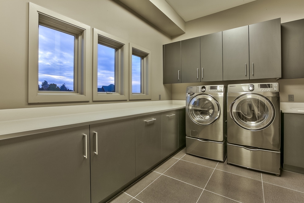 Exempel på en mycket stor modern tvättstuga enbart för tvätt, med släta luckor, grå skåp, bänkskiva i kvartsit, grå väggar och en tvättmaskin och torktumlare bredvid varandra