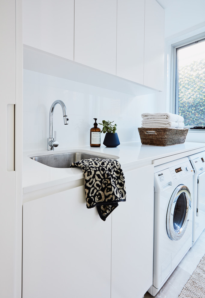 Ispirazione per una lavanderia contemporanea con lavello sottopiano, ante lisce, top in marmo, pareti bianche, lavatrice e asciugatrice affiancate e top bianco