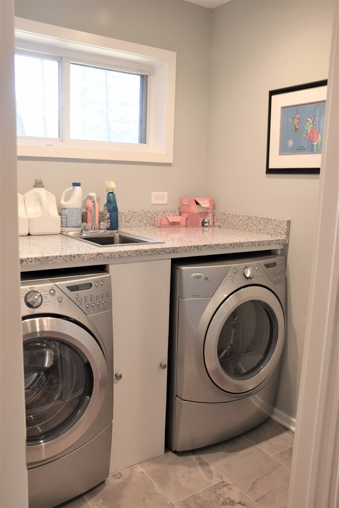 Ejemplo de cuarto de lavado lineal actual pequeño con encimera de granito, paredes grises, suelo de baldosas de porcelana y lavadora y secadora juntas