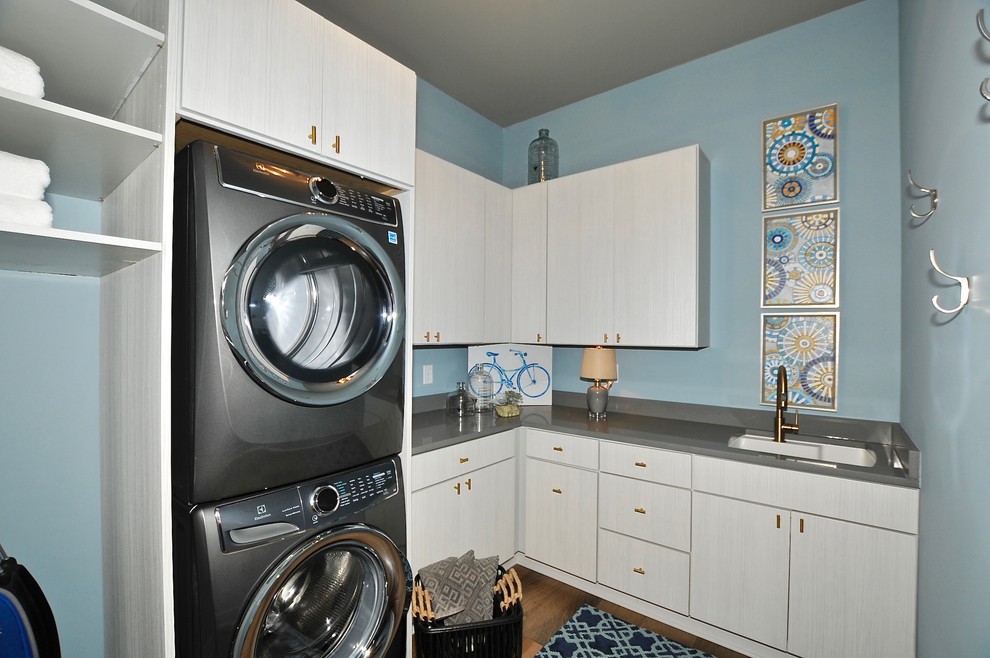 インディアナポリスにある広いコンテンポラリースタイルのおしゃれな洗濯室 (L型、一体型シンク、フラットパネル扉のキャビネット、ベージュのキャビネット、人工大理石カウンター、青い壁、無垢フローリング、上下配置の洗濯機・乾燥機、茶色い床、グレーのキッチンカウンター) の写真