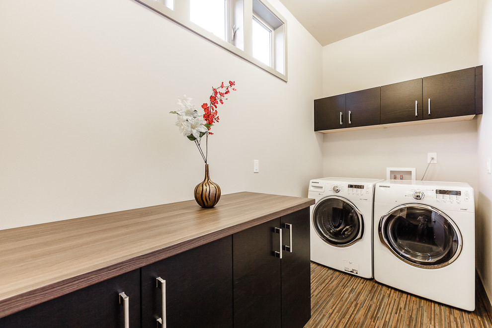 Immagine di una lavanderia multiuso design con ante lisce, top in laminato, pareti beige, pavimento in bambù, lavatrice e asciugatrice nascoste, top marrone e ante in legno bruno