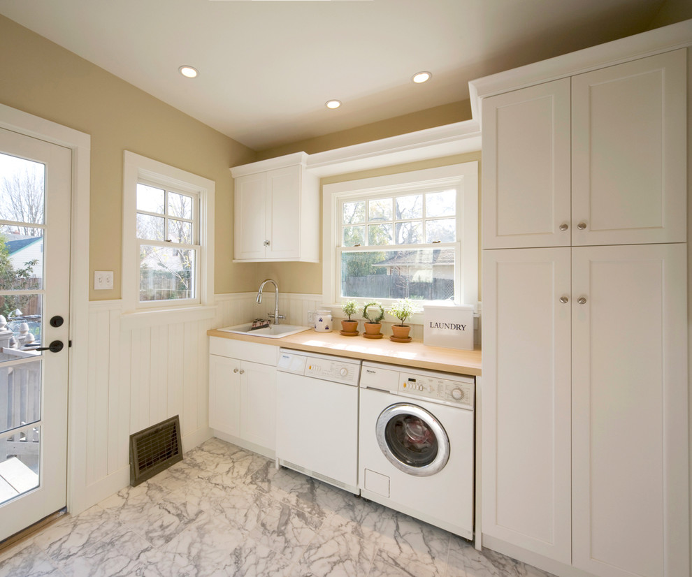 Inspiration for a large timeless single-wall marble floor dedicated laundry room remodel in Sacramento with a drop-in sink, shaker cabinets, white cabinets, wood countertops, beige walls and a side-by-side washer/dryer