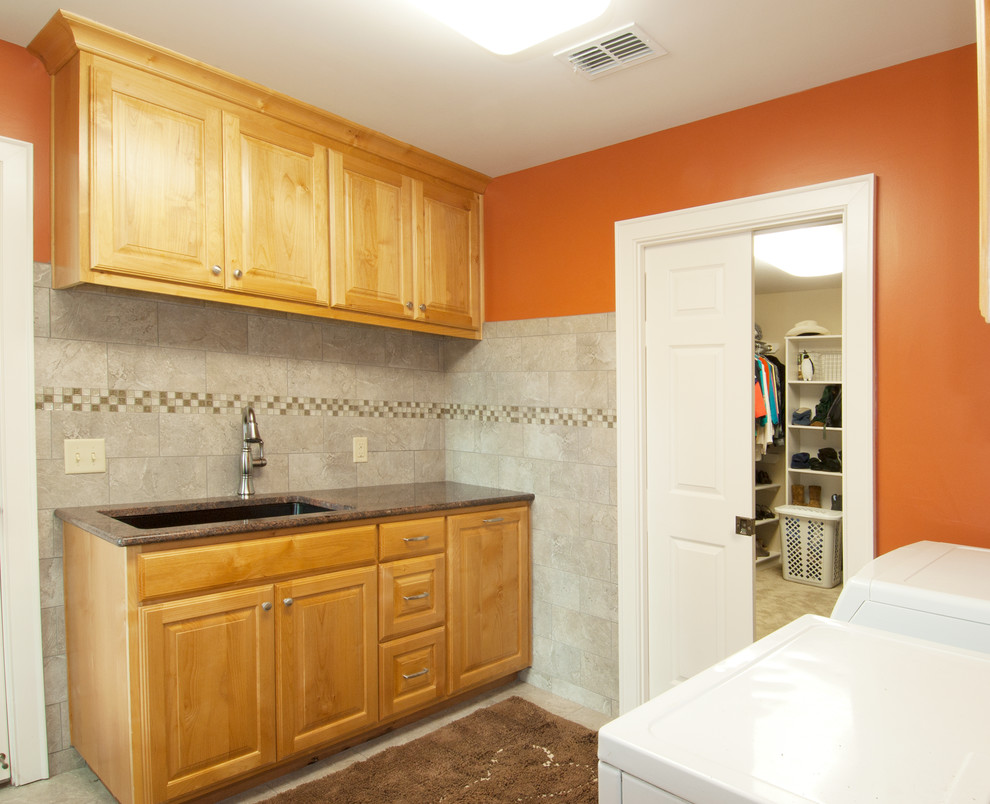 Idéer för en klassisk l-formad tvättstuga enbart för tvätt, med luckor med upphöjd panel, granitbänkskiva, orange väggar, klinkergolv i porslin, en tvättmaskin och torktumlare bredvid varandra och skåp i mellenmörkt trä