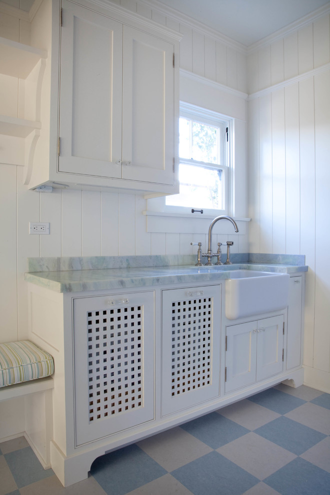 Beach style galley separated utility room in San Diego with a belfast sink, shaker cabinets, white cabinets, marble worktops, white walls and a stacked washer and dryer.