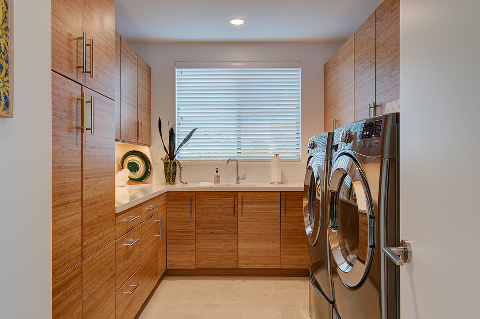 Bild på en funkis vita u-formad vitt tvättstuga enbart för tvätt, med släta luckor, vita väggar, en tvättmaskin och torktumlare bredvid varandra, beiget golv och skåp i mellenmörkt trä