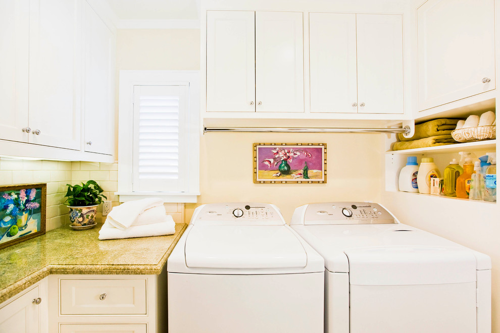 Diseño de cuarto de lavado en U tradicional con armarios con rebordes decorativos, puertas de armario blancas, paredes blancas, lavadora y secadora juntas, encimeras verdes y encimera de granito