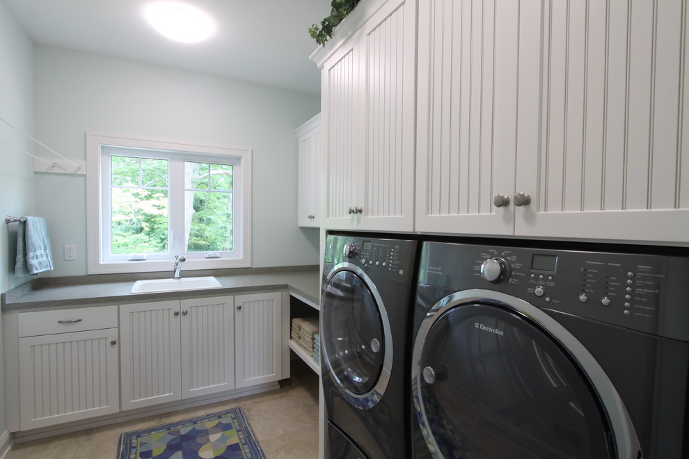 Foto på en lantlig l-formad tvättstuga, med en nedsänkt diskho, luckor med profilerade fronter, vita skåp, klinkergolv i keramik och en tvättmaskin och torktumlare bredvid varandra