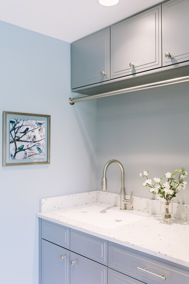 Foto på en vintage tvättstuga, med bänkskiva i återvunnet glas, klinkergolv i porslin, en undermonterad diskho, blå väggar, en tvättmaskin och torktumlare bredvid varandra och grå skåp