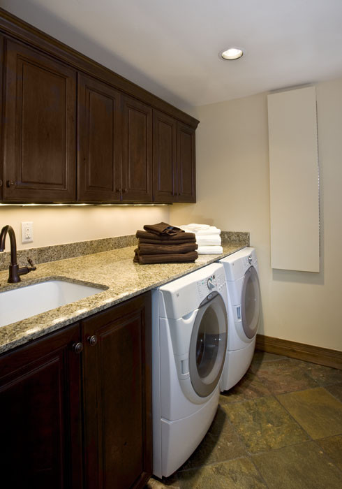 Exempel på en stor klassisk linjär tvättstuga enbart för tvätt, med en undermonterad diskho, luckor med upphöjd panel, skåp i mörkt trä, granitbänkskiva, beige väggar, skiffergolv och en tvättmaskin och torktumlare bredvid varandra