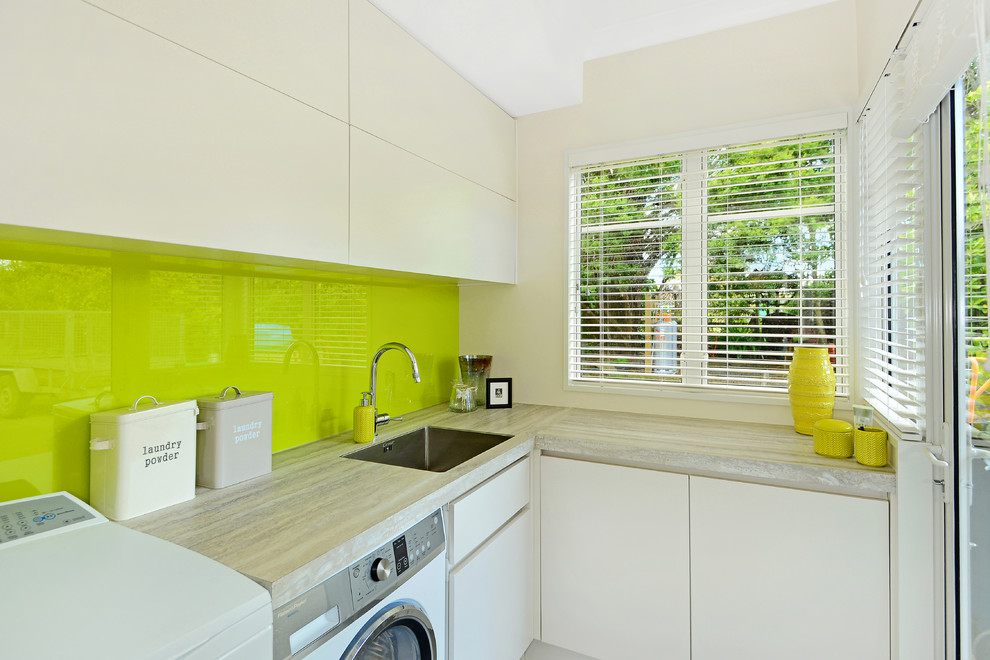 Kleine Moderne Waschküche in L-Form mit Waschbecken, flächenbündigen Schrankfronten, weißen Schränken, Laminat-Arbeitsplatte, weißer Wandfarbe und Waschmaschine und Trockner nebeneinander in Auckland