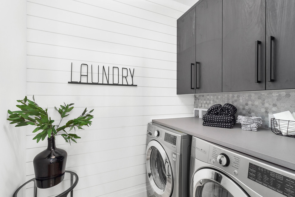 Bild på en funkis grå grått tvättstuga, med släta luckor, svarta skåp, bänkskiva i kvarts och en tvättmaskin och torktumlare bredvid varandra